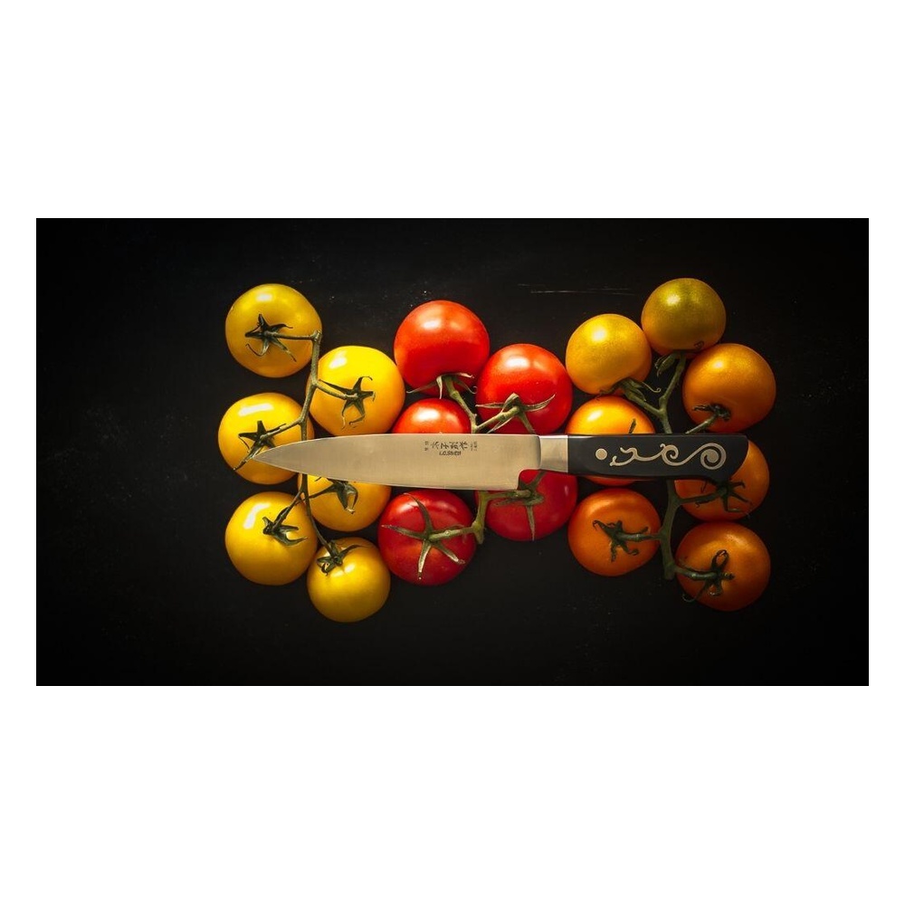 Assorted yellow, orange, and red cherry tomatoes on a vine with a decorative knife laid across them on a dark surface