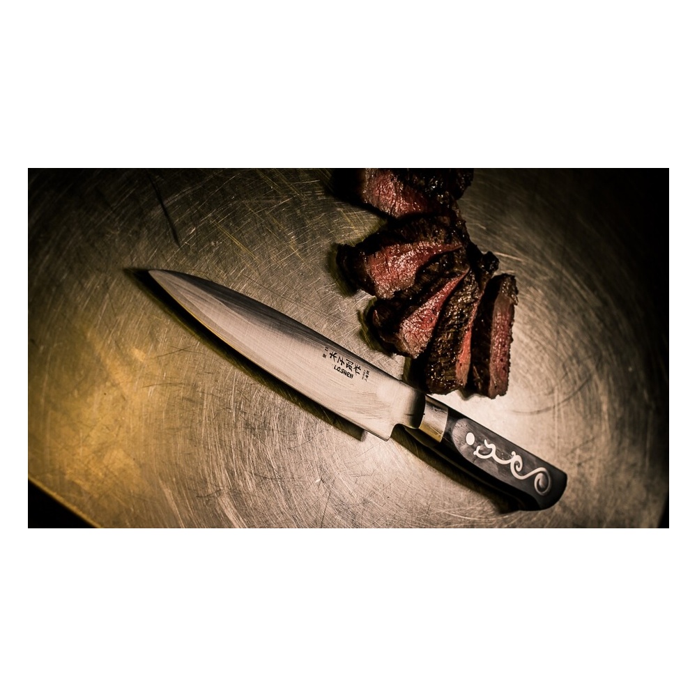Sliced cooked steak beside a large kitchen knife on a scratched metal surface
