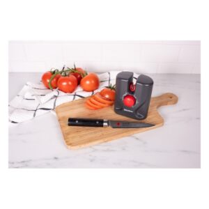 Tomato slicing gadget and knife on a wooden cutting board with fresh tomatoes and a striped towel in a bright kitchen setting.