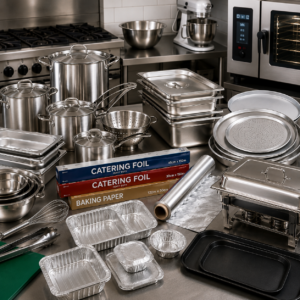 Assorted stainless steel cookware and bakeware on a commercial kitchen counter, including pots, pans, tins, and foil rolls